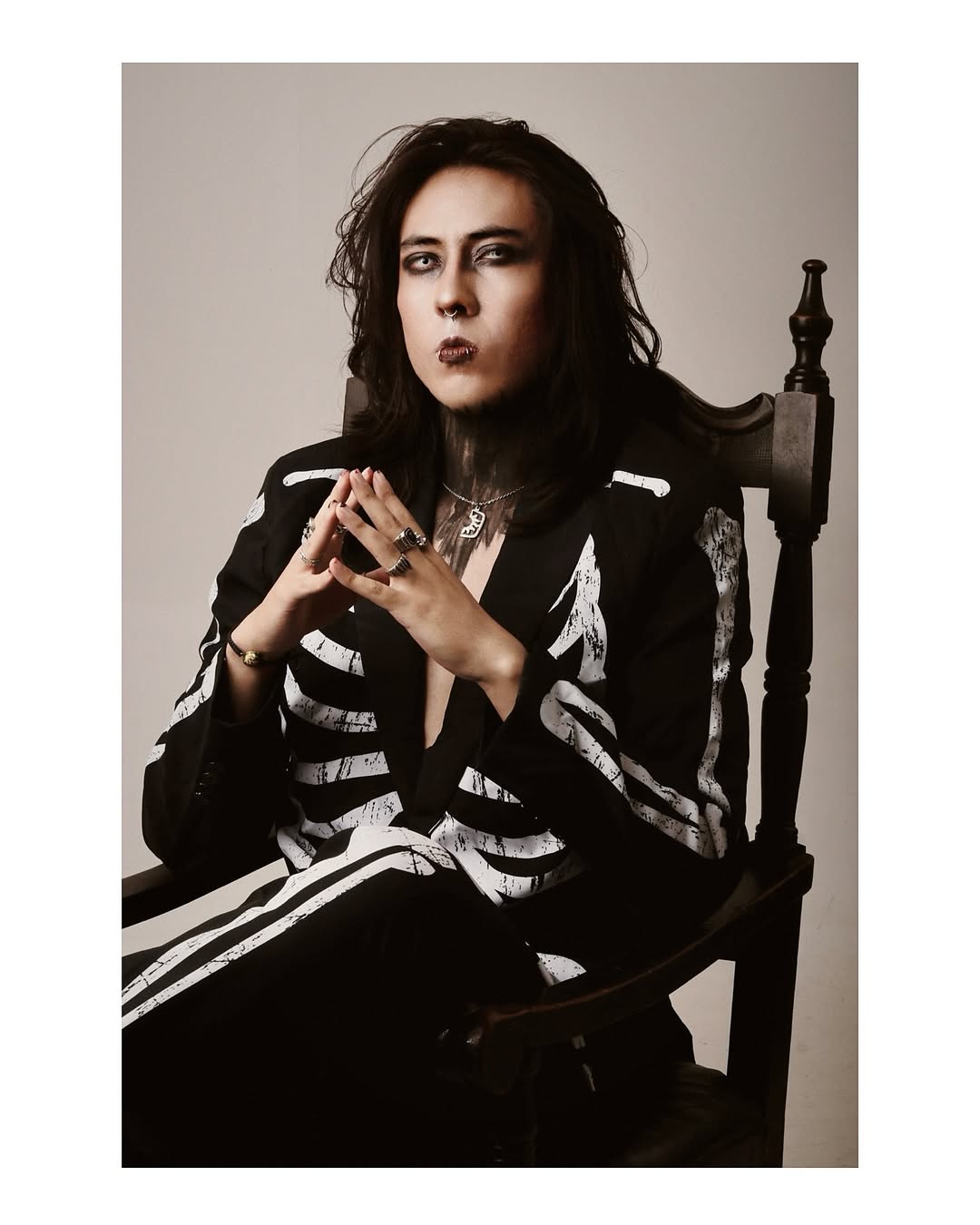 Johan Peraza sitting thoughtfully on a wooden chair in a dark moody jacket with hands together