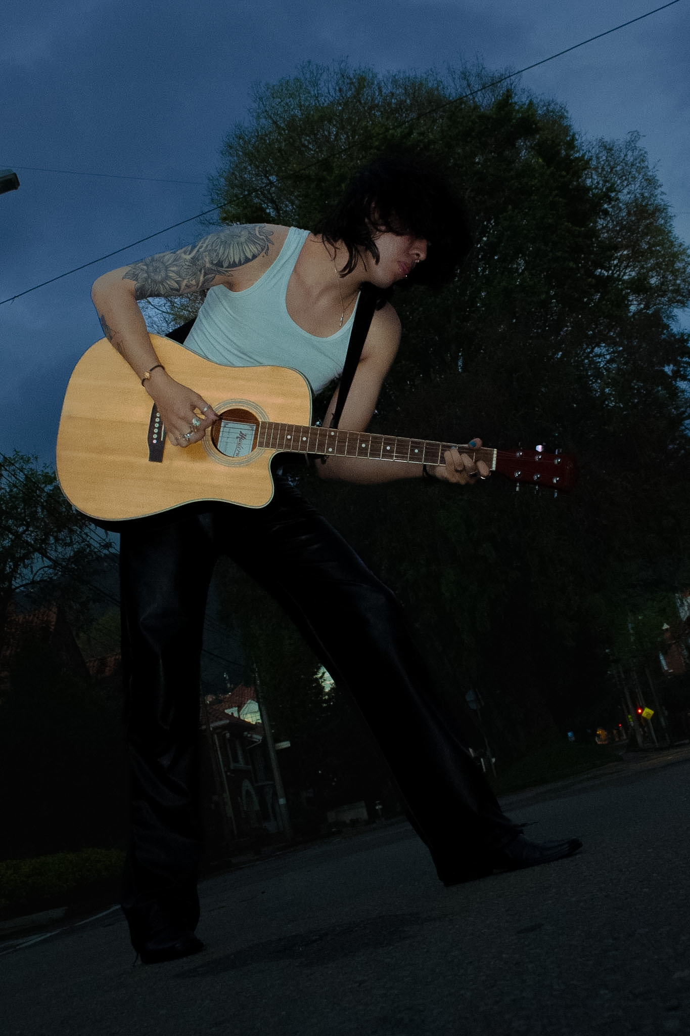 Johan Peraza, wide full-length shot playing acoustic guitar outdoors at dusk