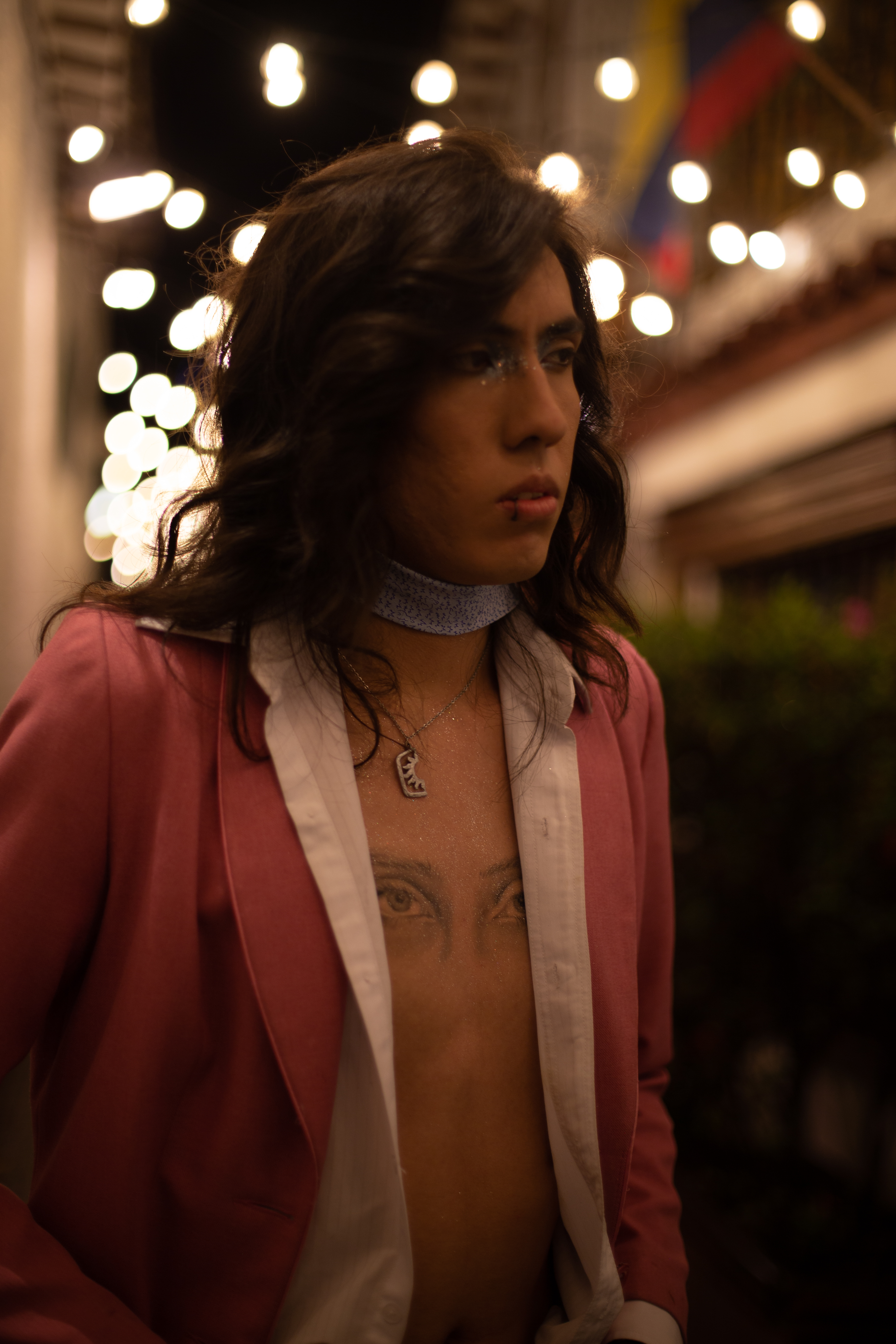 Johan Peraza, editorial fashion portrait in a pink blazer showcasing chest tattoos under warm city lights