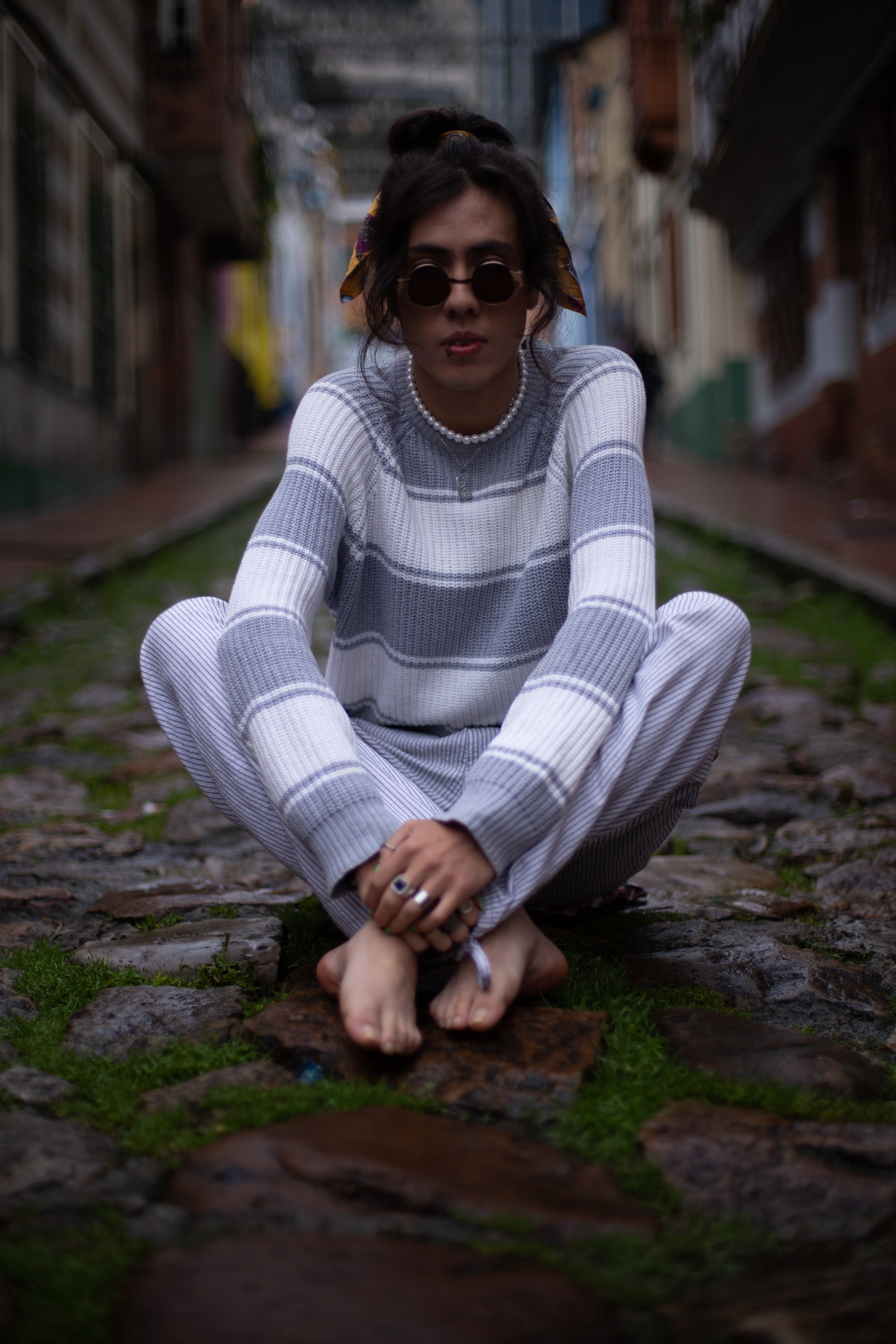 Johan Peraza, full-length portrait sitting on a rustic cobblestone street wearing a striped knit jumper