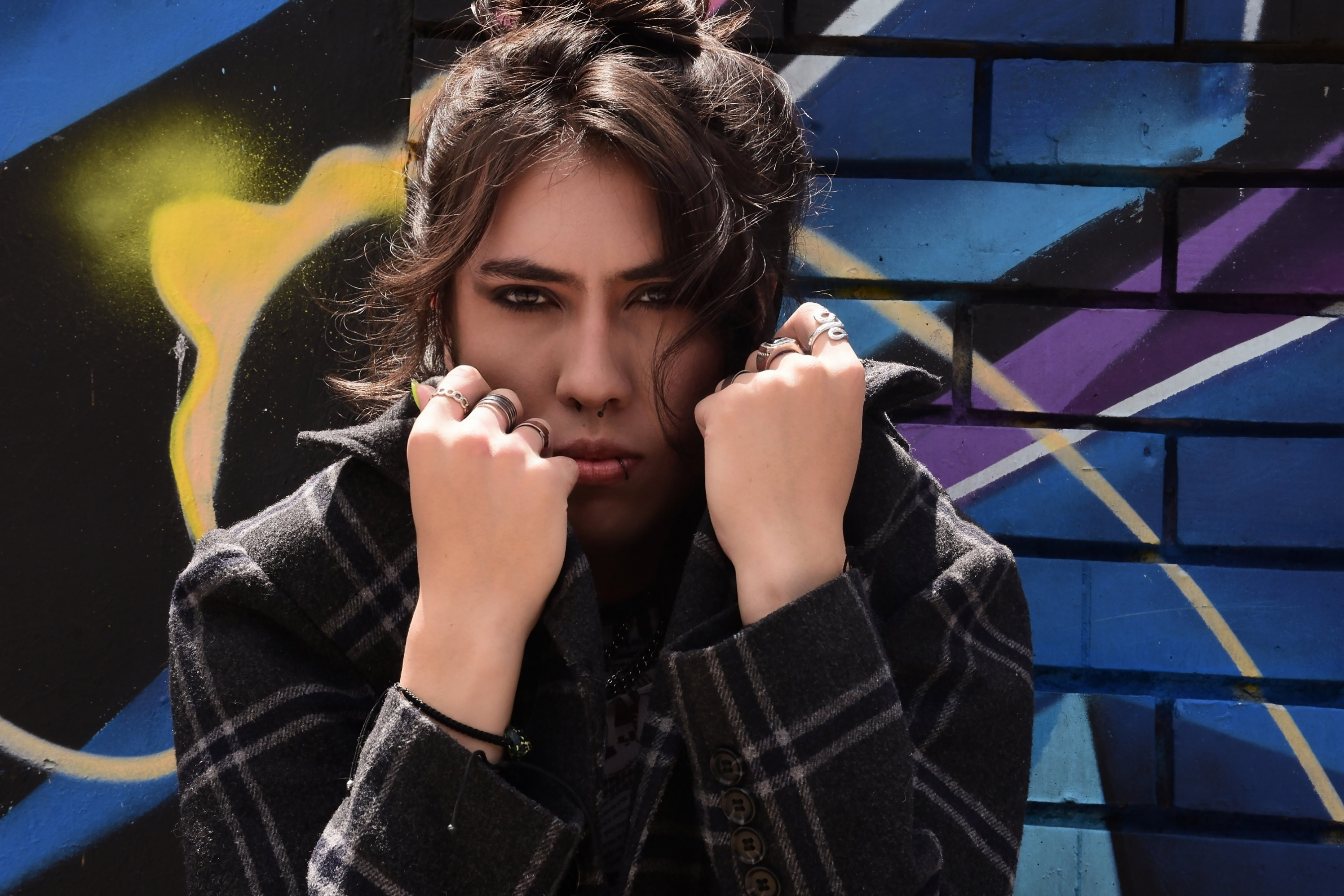 Johan Peraza, medium shot posing in a checkered jacket against a graffiti wall background