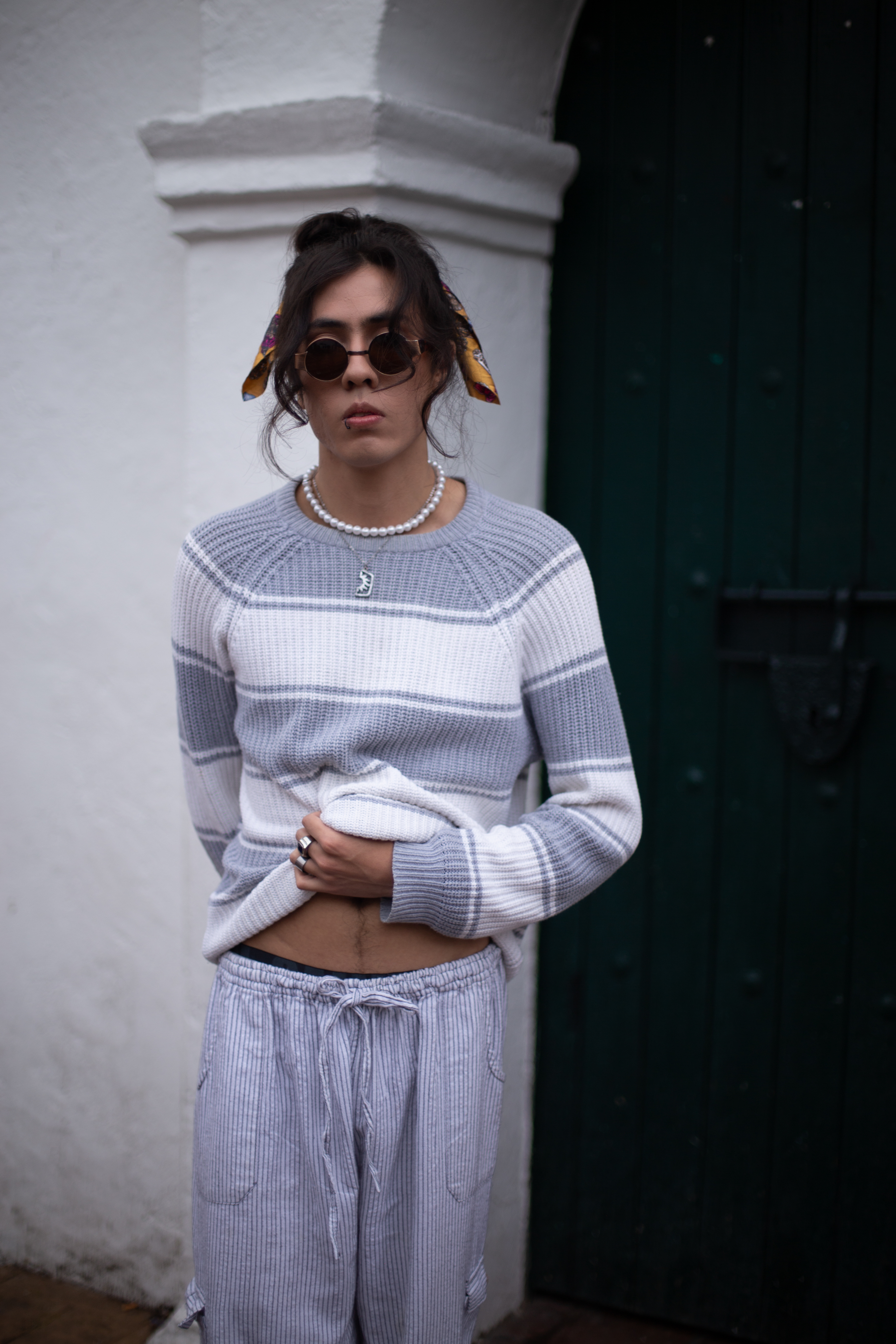 Johan Peraza, outdoor full-length portrait in casual knitwear and sunglasses against a clean wall